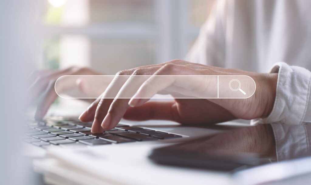 image of hands typing on a laptop computer with a search bar overlayed